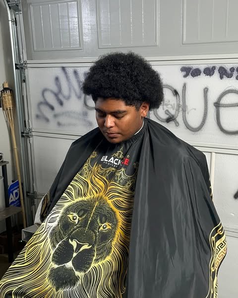 Full afro shaped up with tapered sides, against the CRITIQUE wall